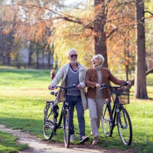 old couple strolling through park with their eBikes